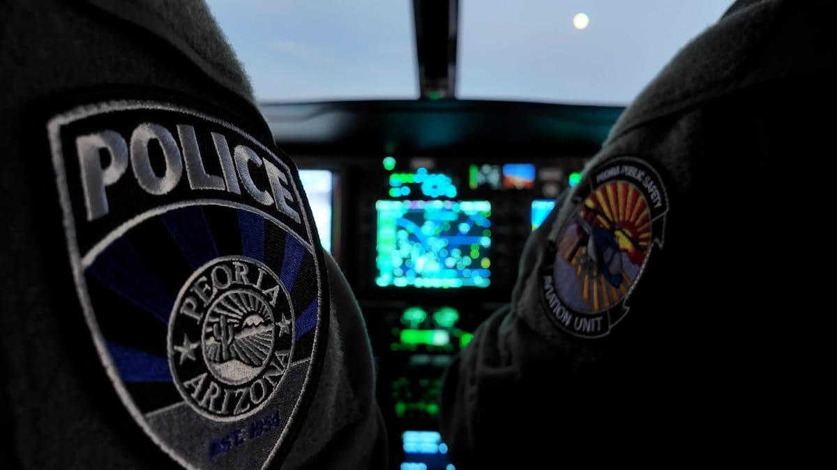 Two police officers in a cockpit, one in a Peoria, Arizona uniform, with flight instruments visible.
