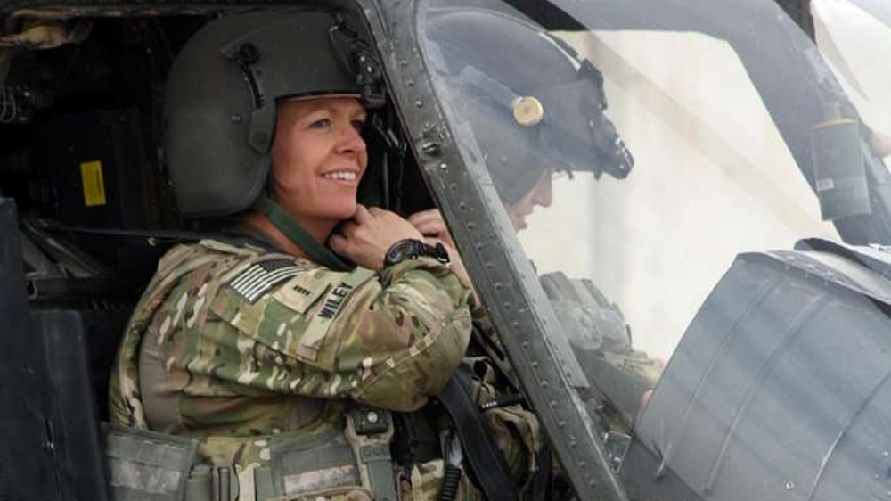 Military service member in cockpit of a helicopter, smiling while adjusting her headset.