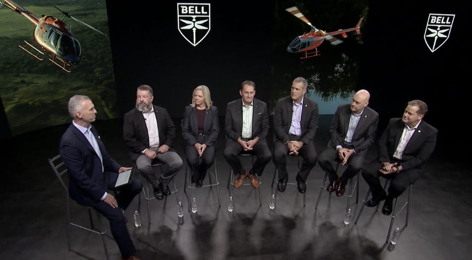 A panel of six people seated on stools, discussing aviation, with Bell helicopters displayed in the