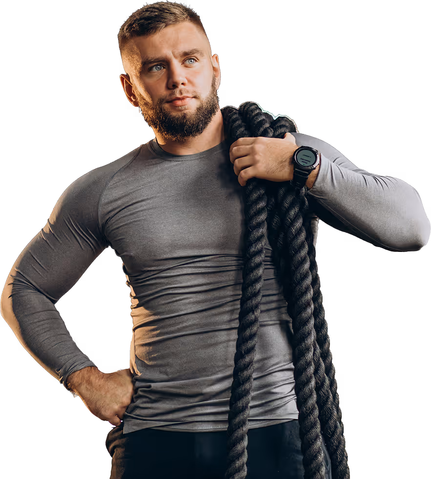 Fit bearded man in a gray long-sleeve shirt holding heavy black battle ropes over his shoulder.