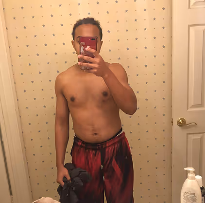 Shirtless man taking a mirror selfie in a bathroom with star-patterned wallpaper and a white door.