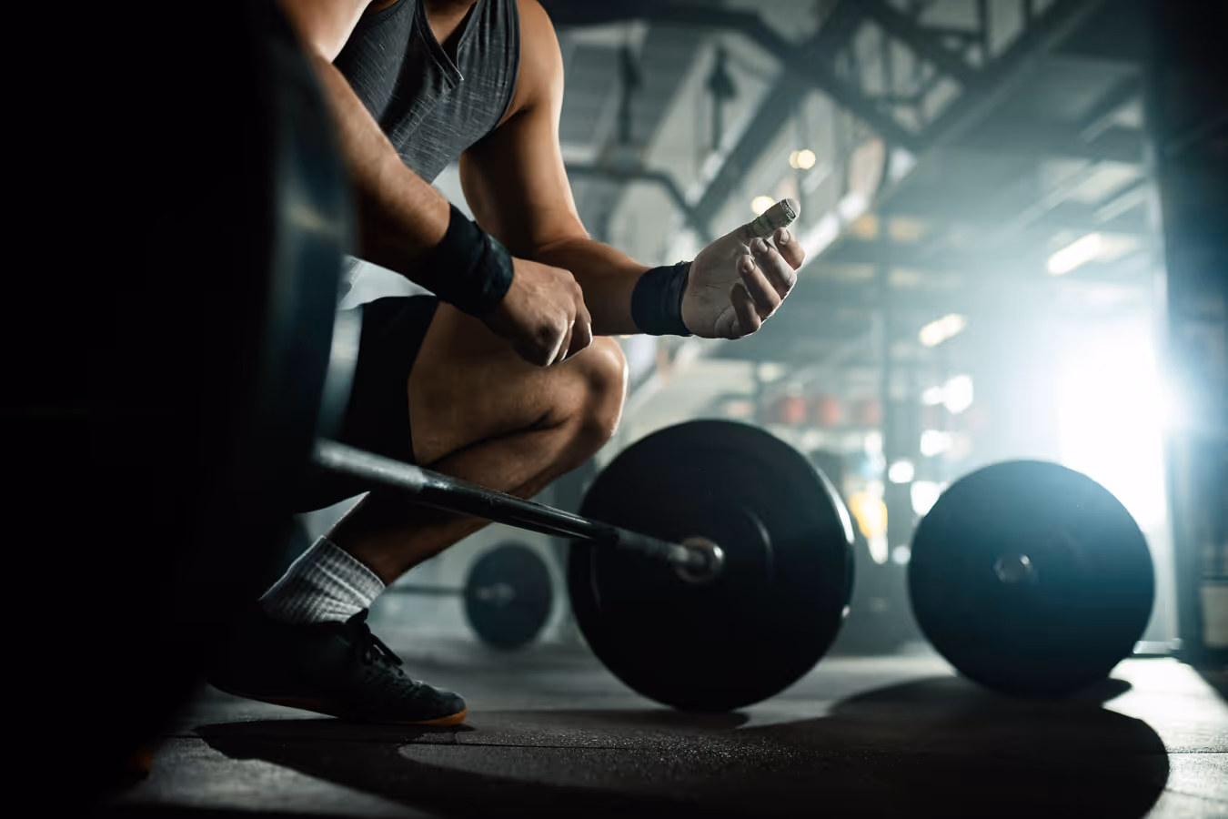 Athlete in wrist wraps preparing to lift a loaded barbell in a gym setting.