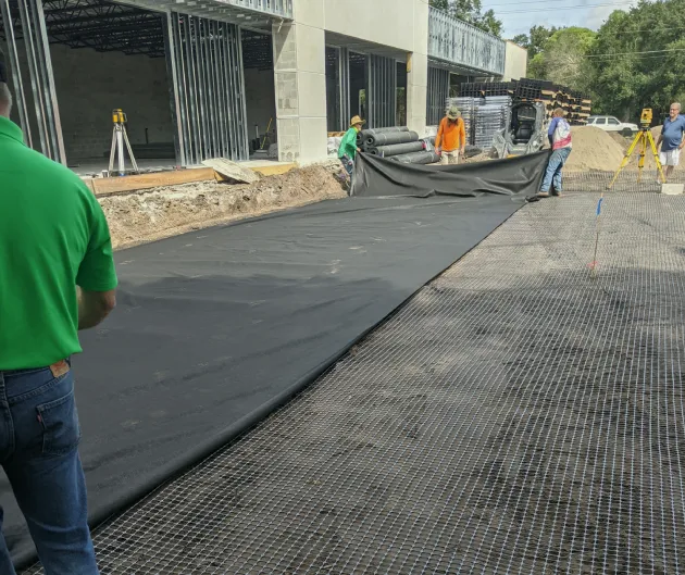 Crew laying geotextile fabric over grid at a commercial construction site