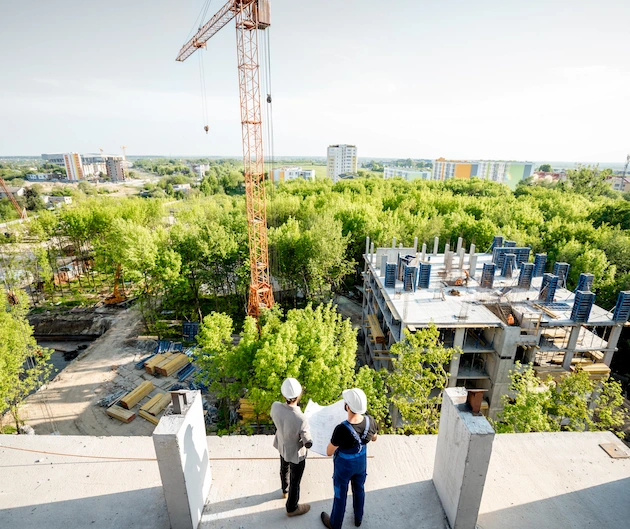 Two workers look out over a construction site with trees