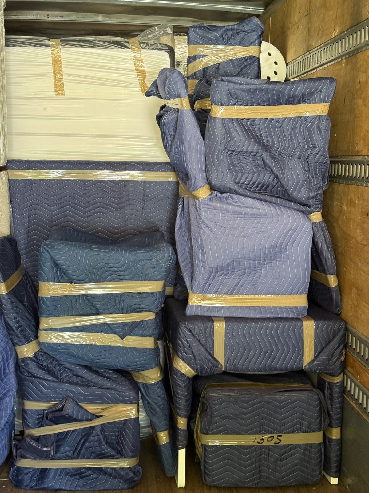 Furniture pieces wrapped in protective blue moving blankets and secured with packing tape inside a truck.