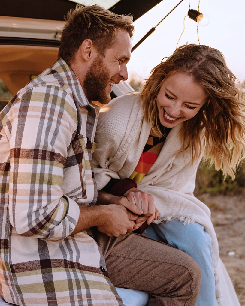 Smiling couple sitting closely together outdoors, holding hands and enjoying a moment of laughter.