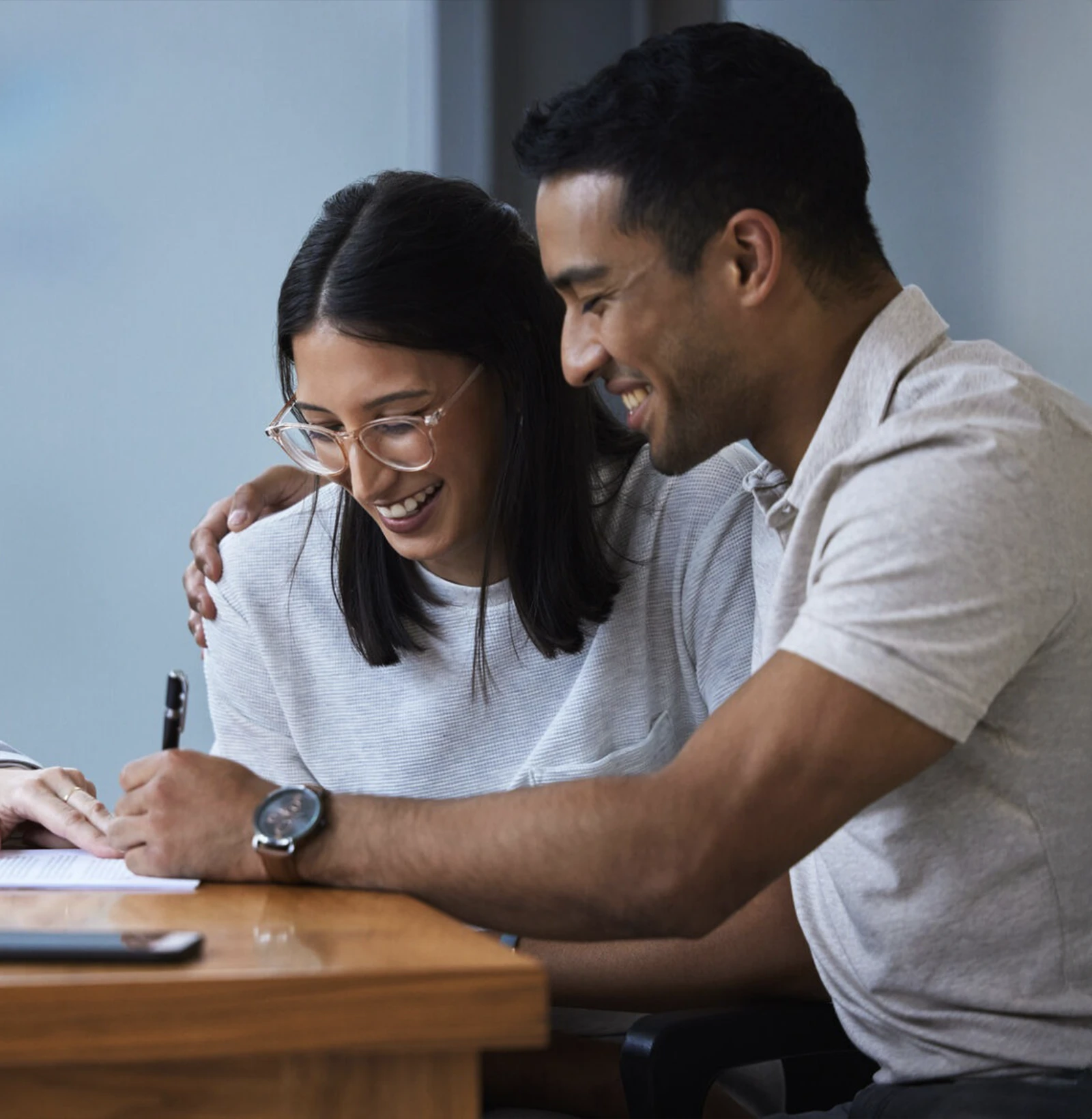 Smiling couple reviewing and signing a document together at a wooden table.