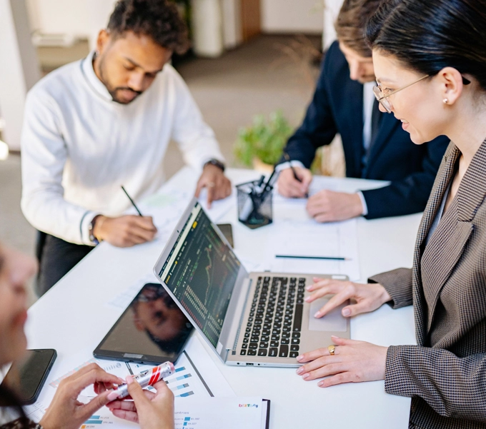 A group of professionals collaborating around a table with a laptop displaying financial charts and documents with graphs.