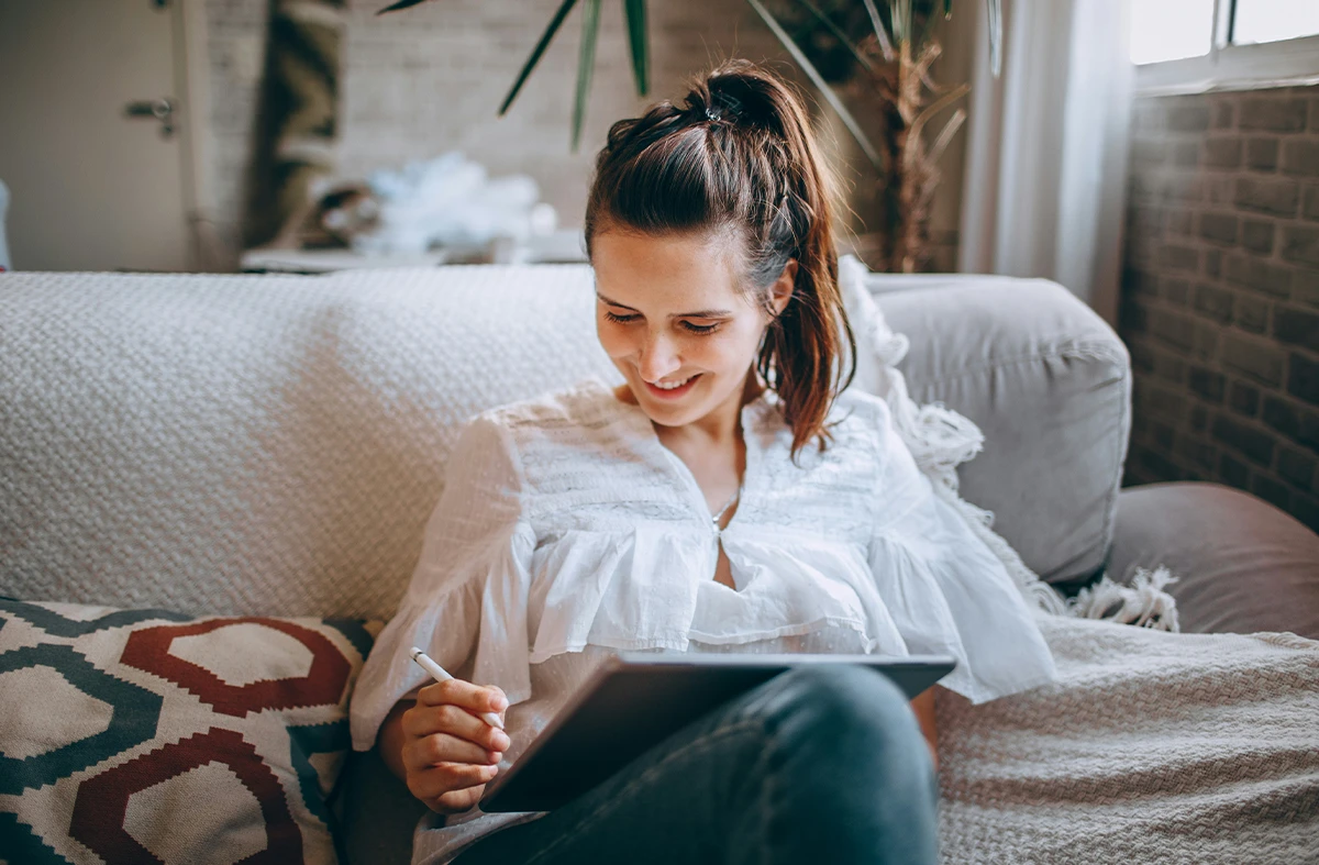A pregnant woman sits on her couch using an ipad.