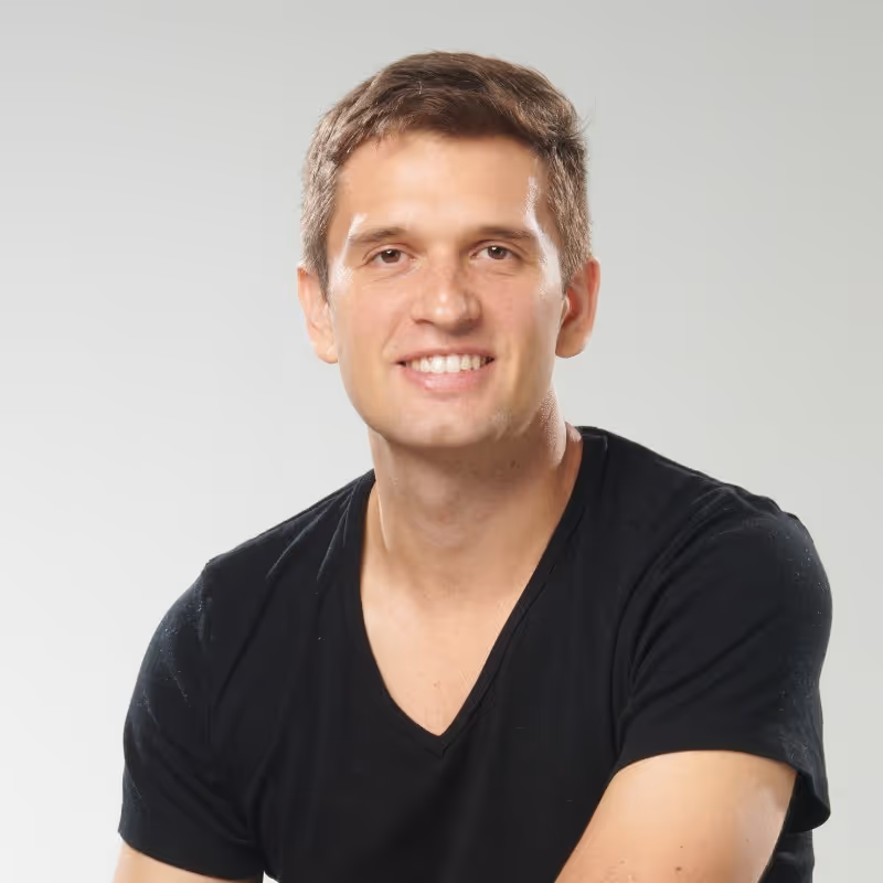 Smiling young man wearing a black V-neck T-shirt against a plain light background.