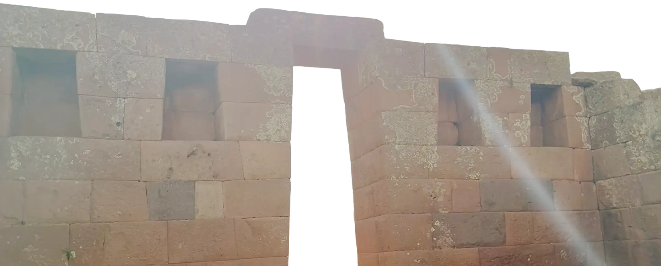 Ancient stone wall with a trapezoidal doorway and three trapezoidal windows, showing weathered stones with lichen patches.