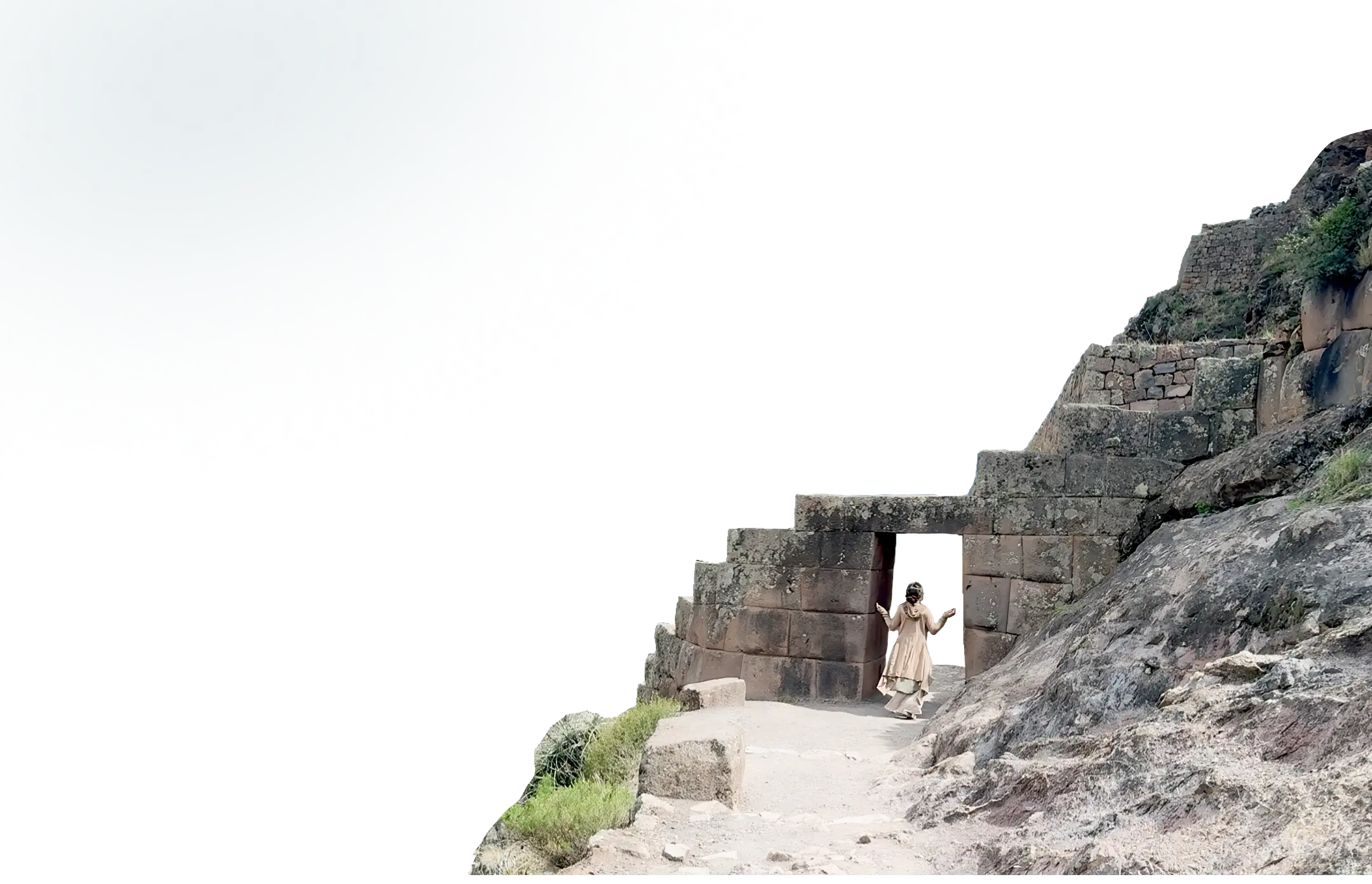 Person in beige outfit walking through an ancient stone doorway carved into rocky terrain.