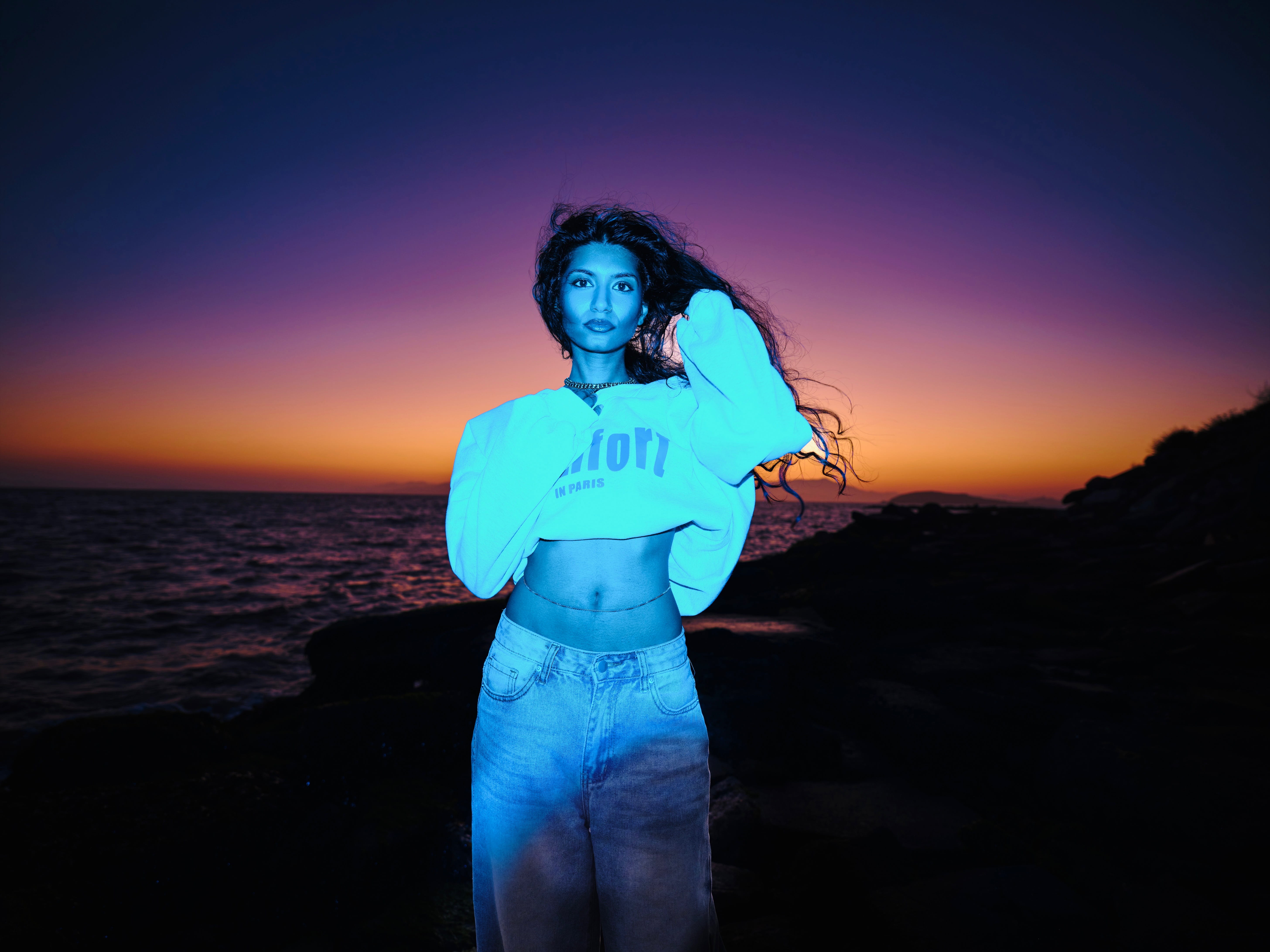 Person standing by the ocean at sunset with colorful sky in the background