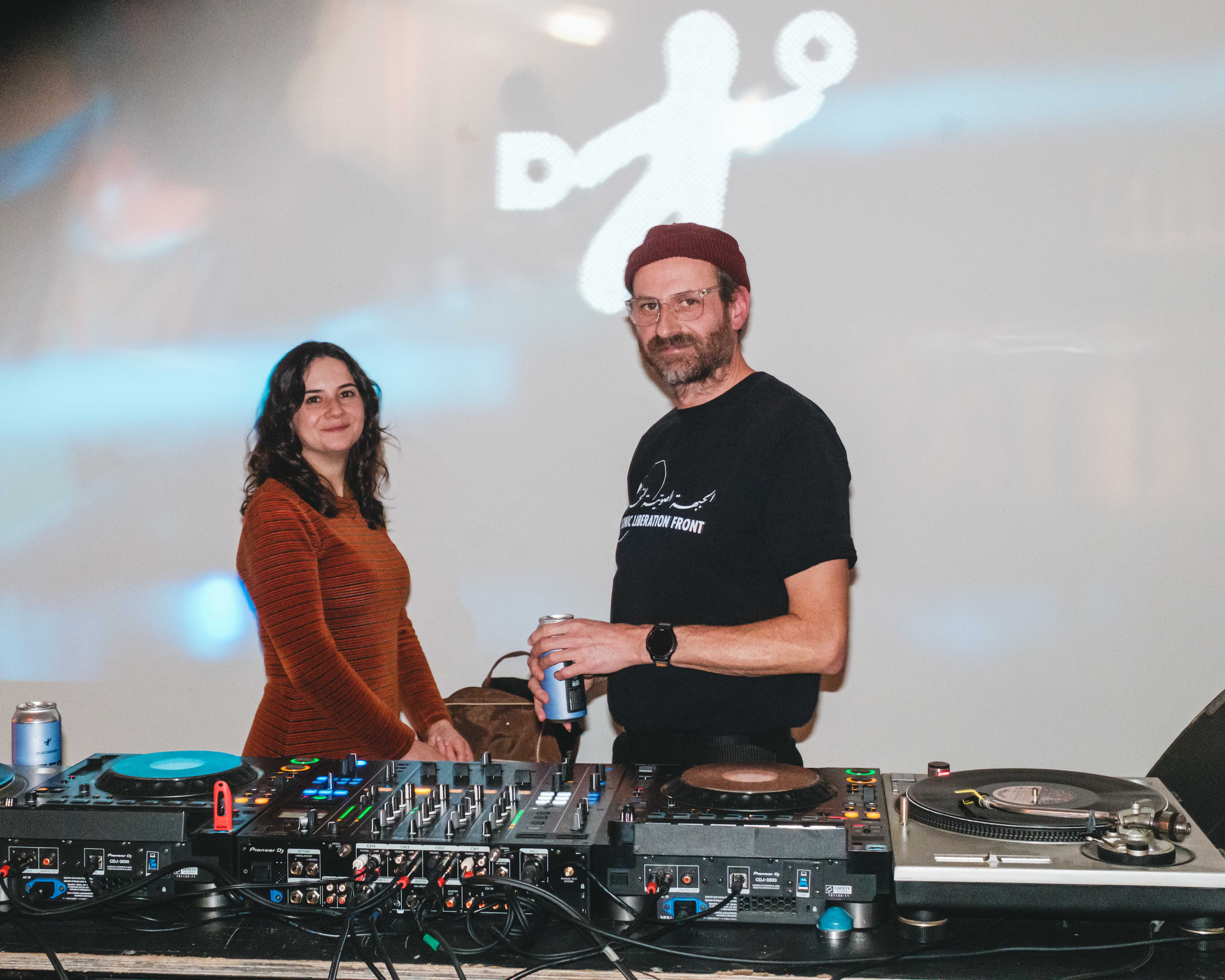 Two people stand behind a DJ booth