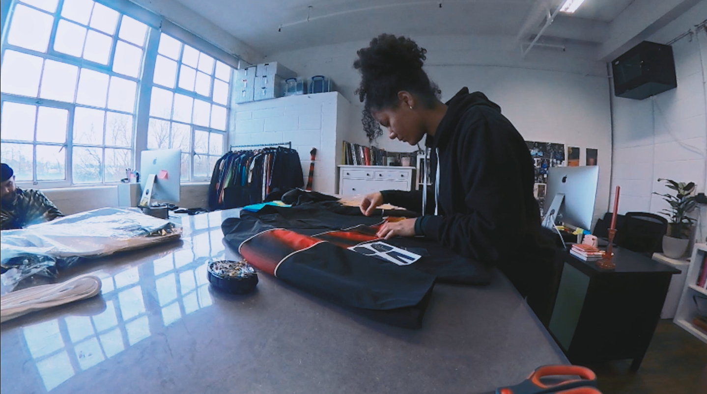 Person working on folded clothing at a table in a bright studio workspace.