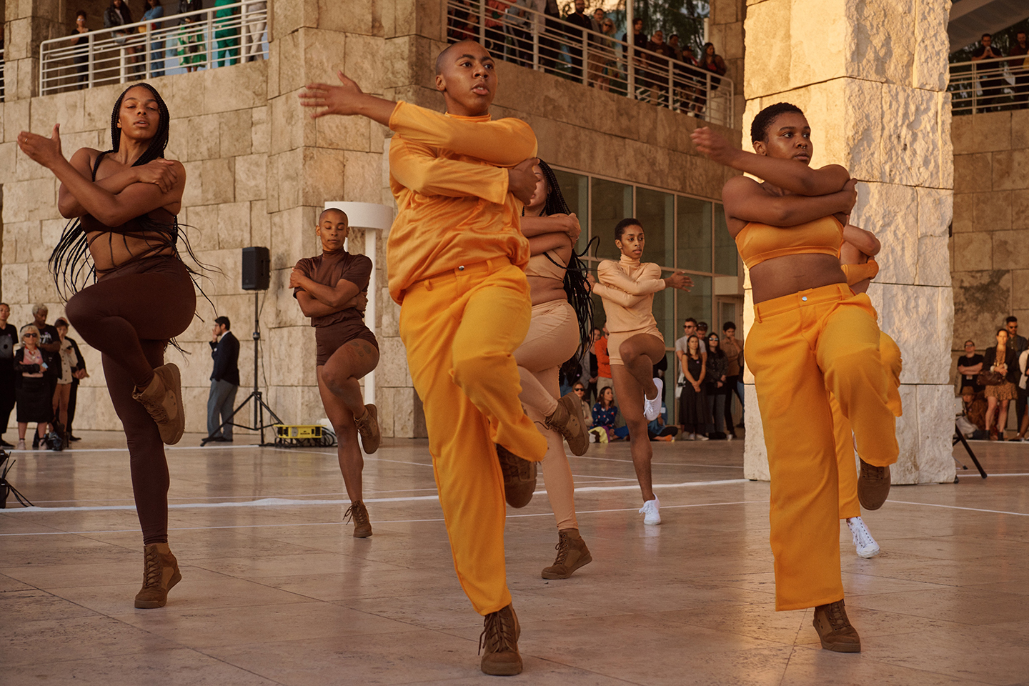 Dance group performing outdoors in coordinated earth-tone outfits before a crowd.