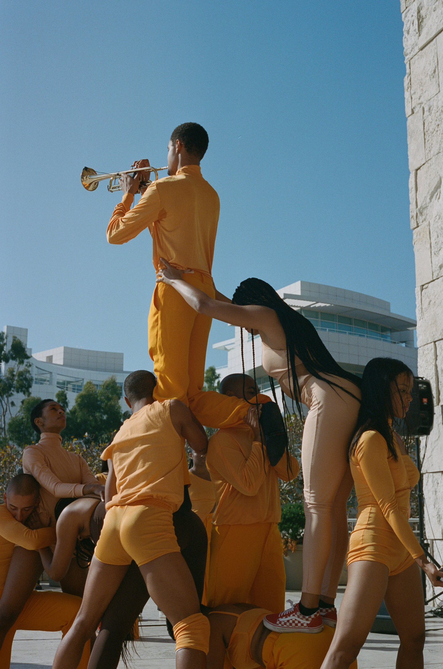 Group of dancers in orange forming a human structure around a trumpet player