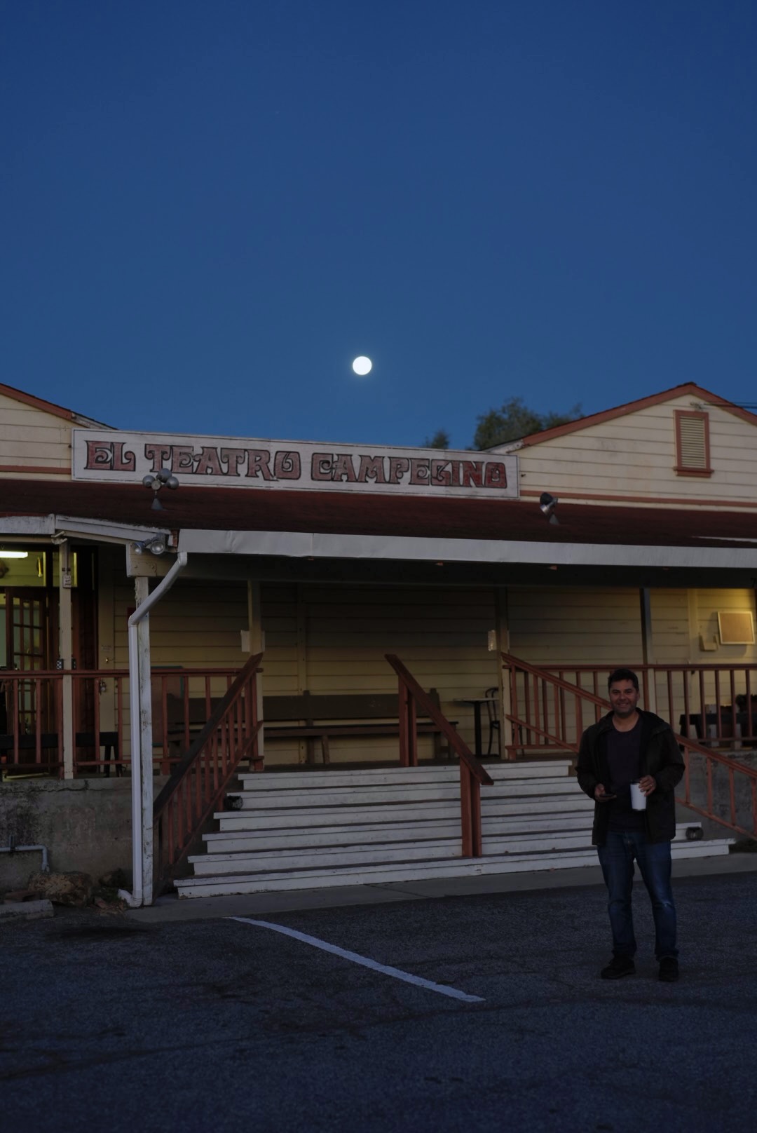 Person standing outside a building at dusk with the moon overhead