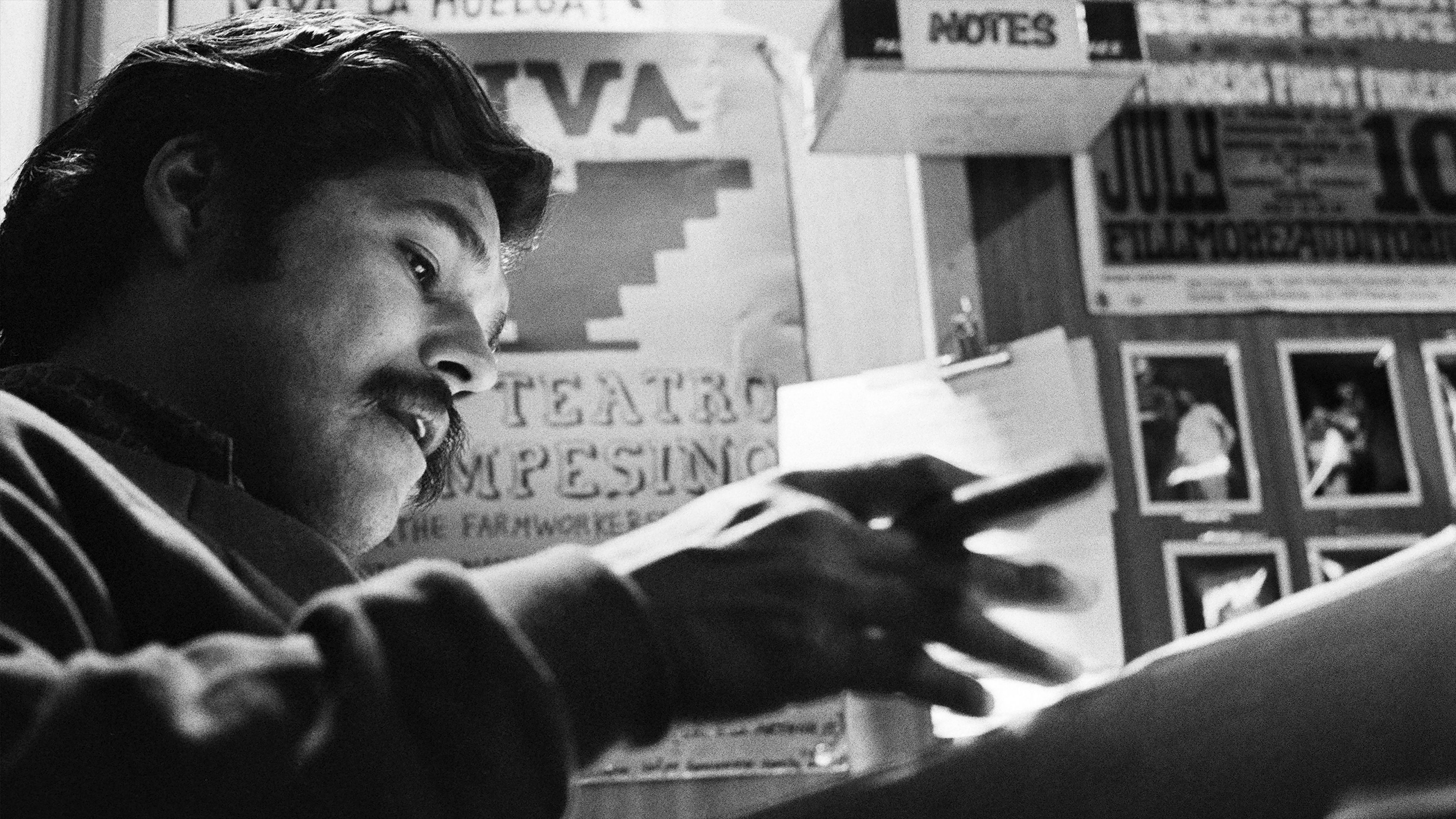Man writing on paper at a desk with posters and photos on the wall