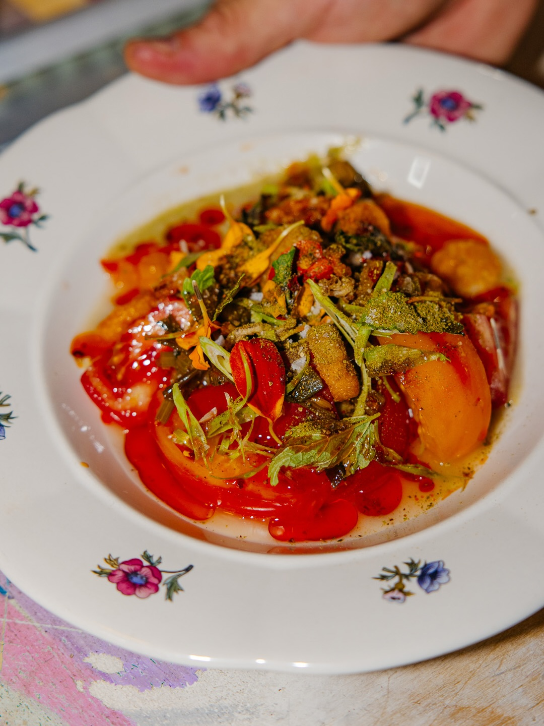 Close-up of a plated tomato salad, served on a white plate with small floral designs.