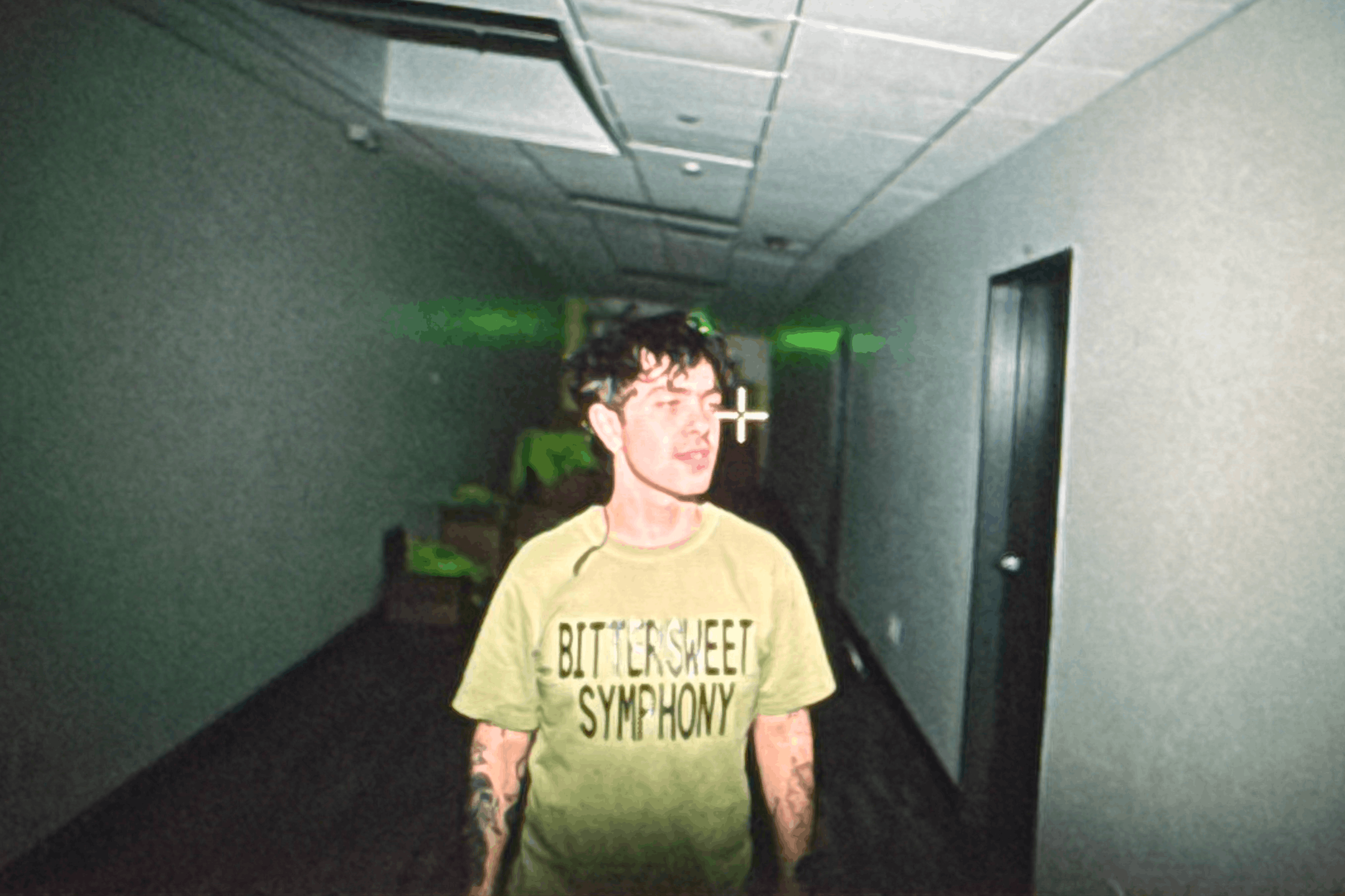 Person in a dim hallway wearing a “Bittersweet Symphony” shirt, looking to the side