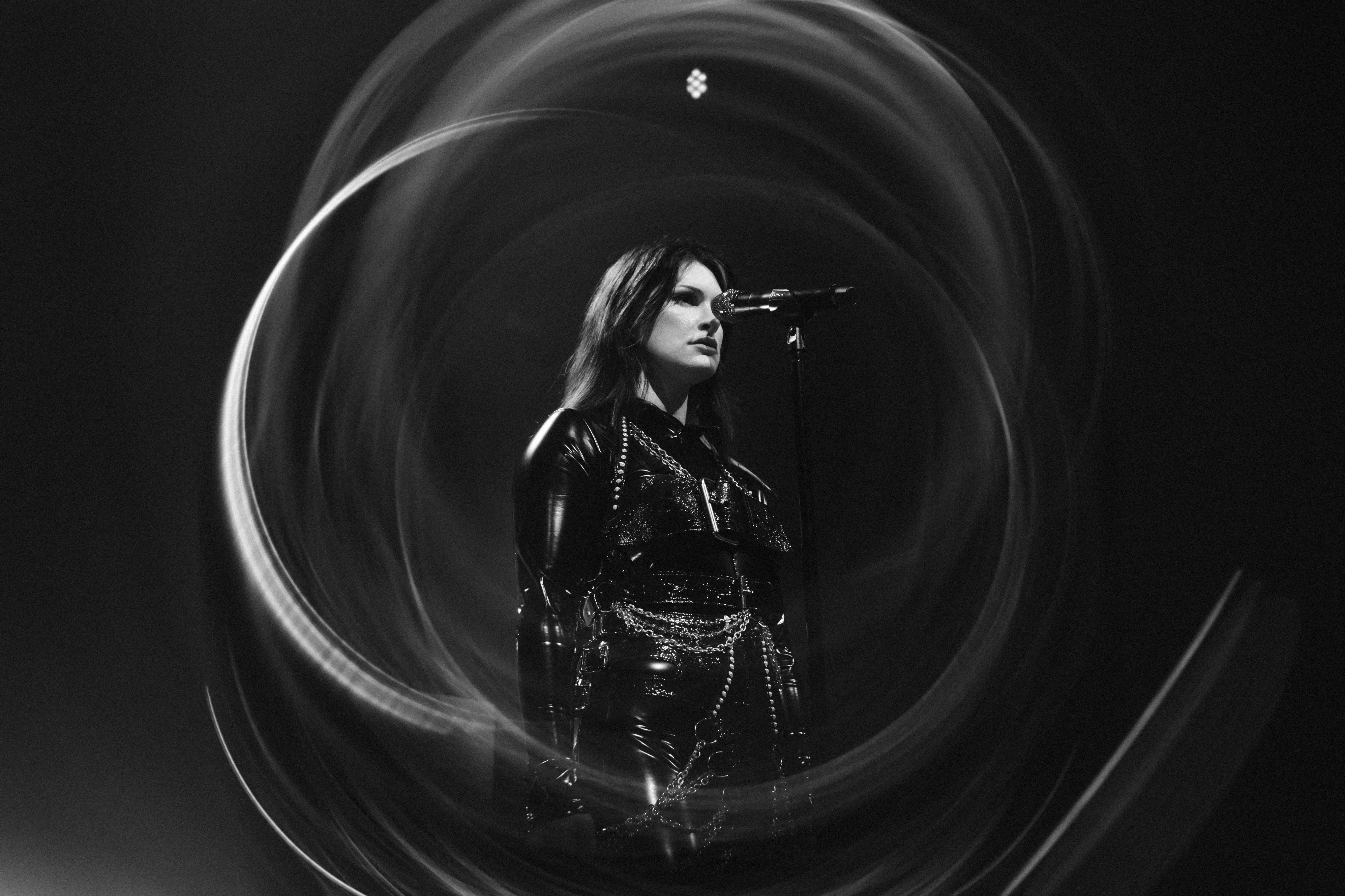 Singer at a microphone surrounded by swirling light effects in a black-and-white scene