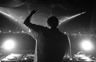 Black-and-white photo of a DJ performing to a crowd with raised hand on stage