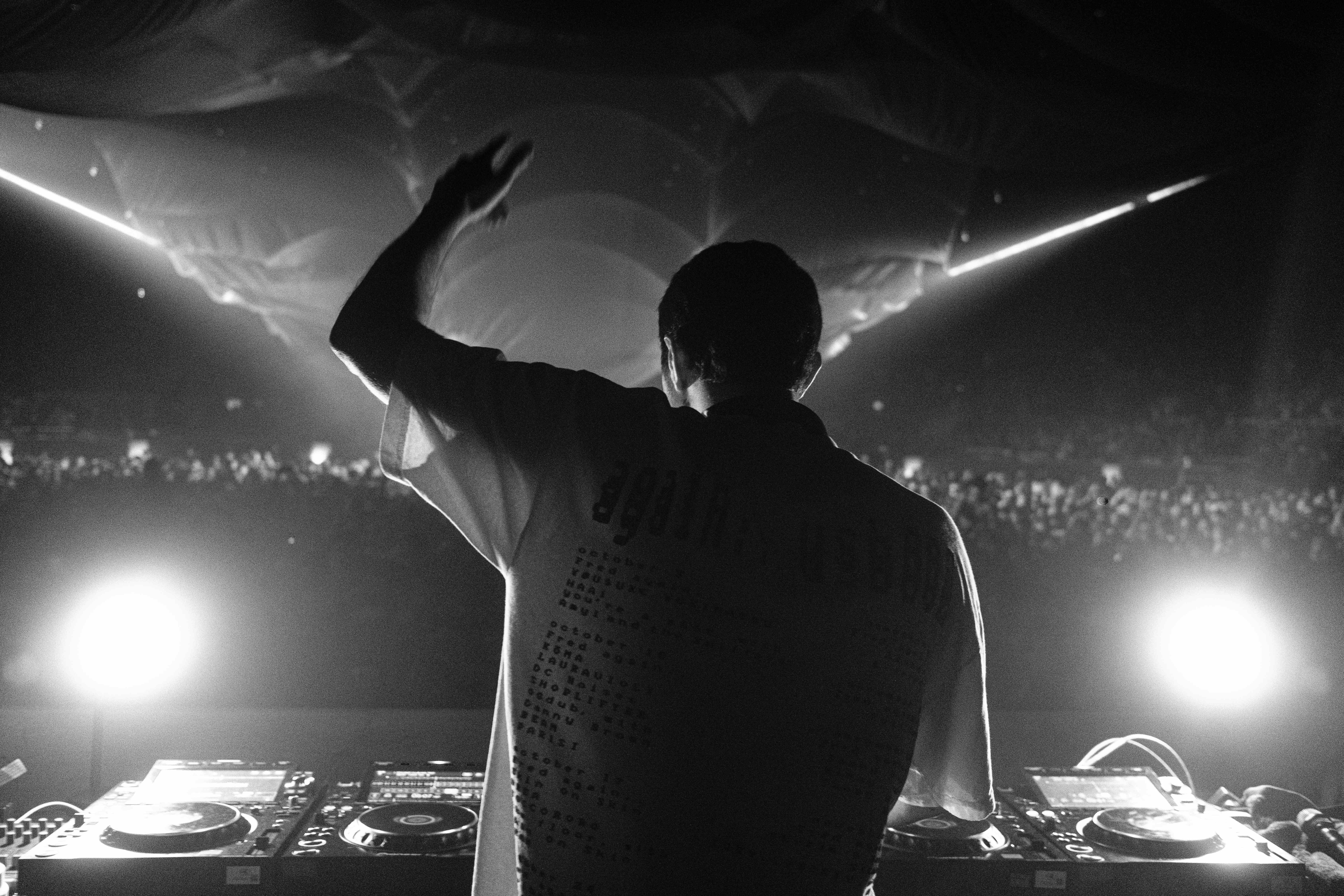 Black-and-white photo of a DJ performing to a crowd with raised hand on stage