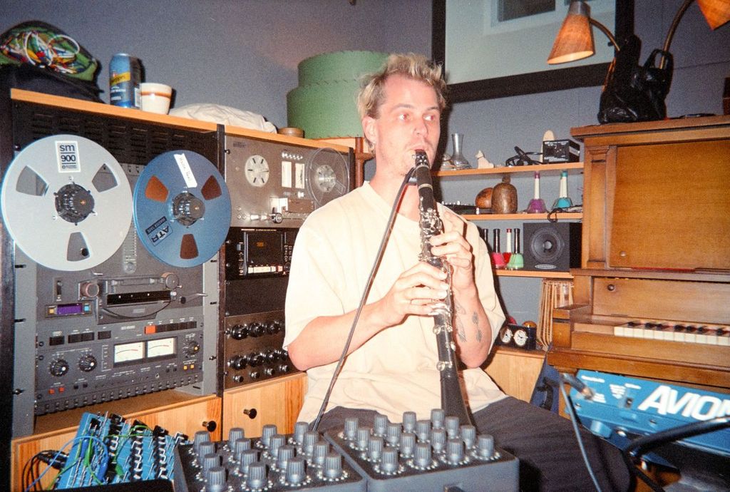 Man playing a clarinet in a recording studio surrounded by audio equipment