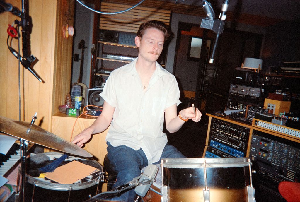 Man playing drums in a recording studio surrounded by microphones and audio equipment