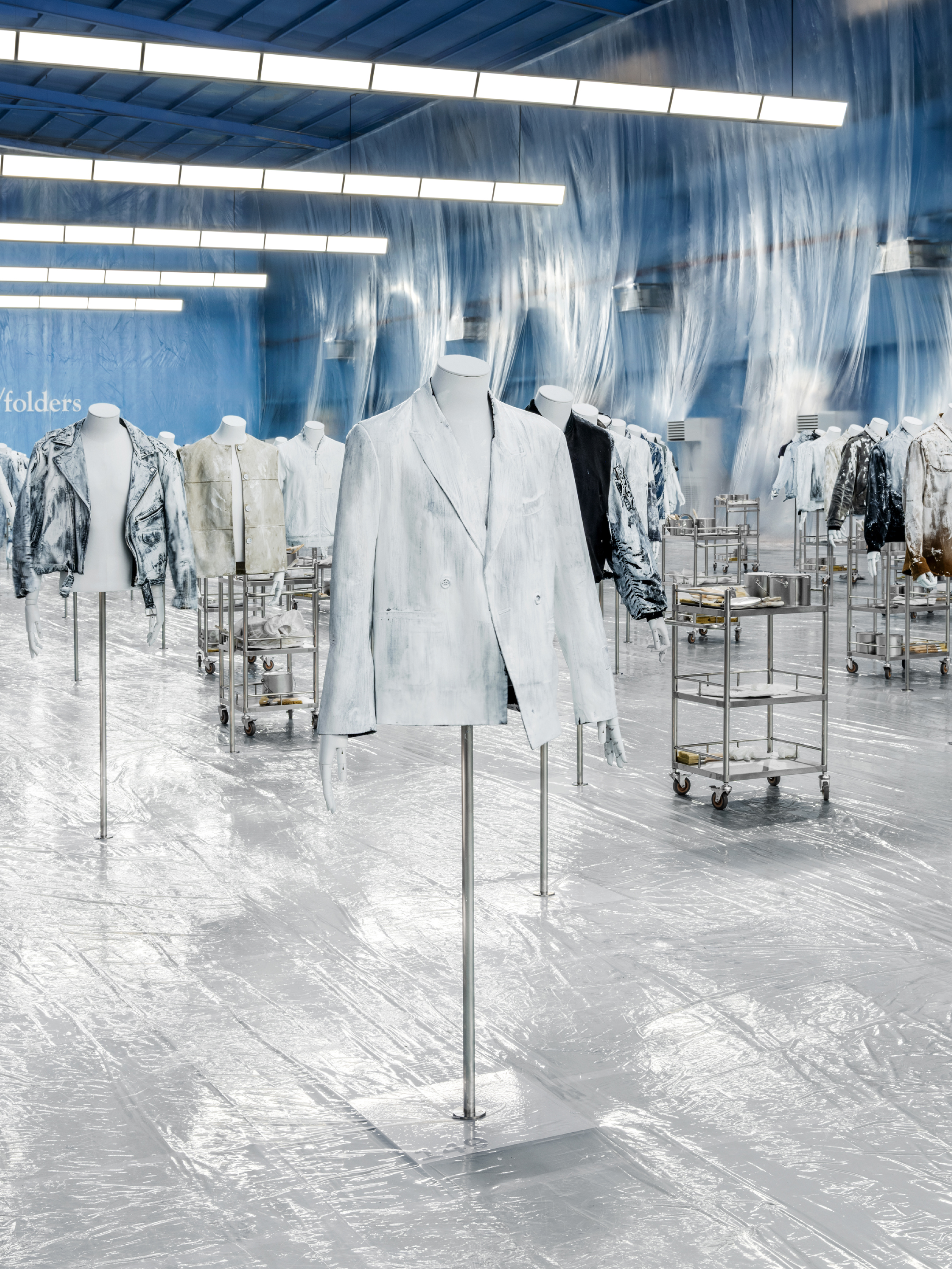 Silver and white jackets on mannequins in a blue showroom with plastic curtains.