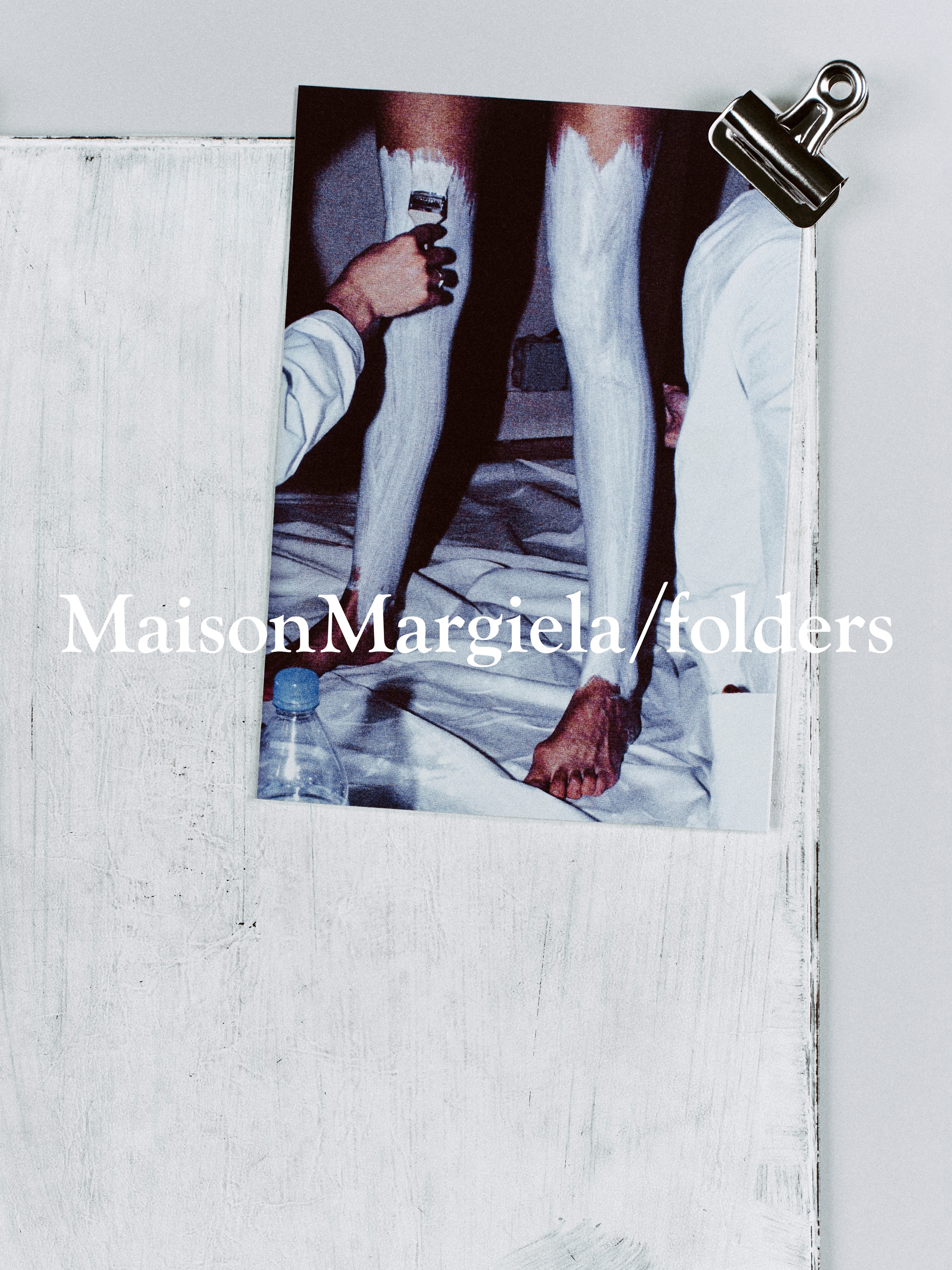 Maison Margiela poster clipped to a white board, showing painted legs and feet.