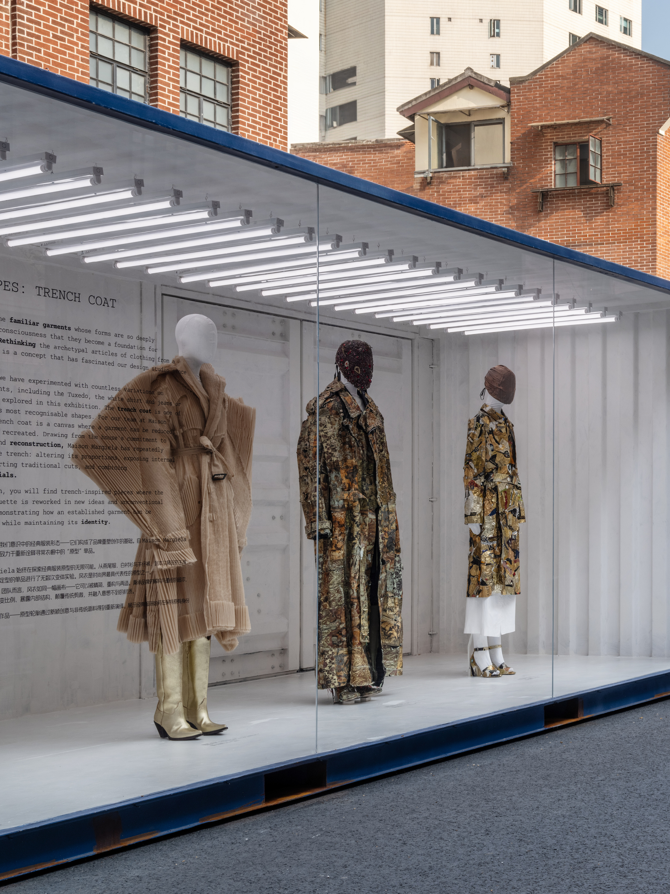 Mannequins displaying designer clothing inside a glass shipping container storefront