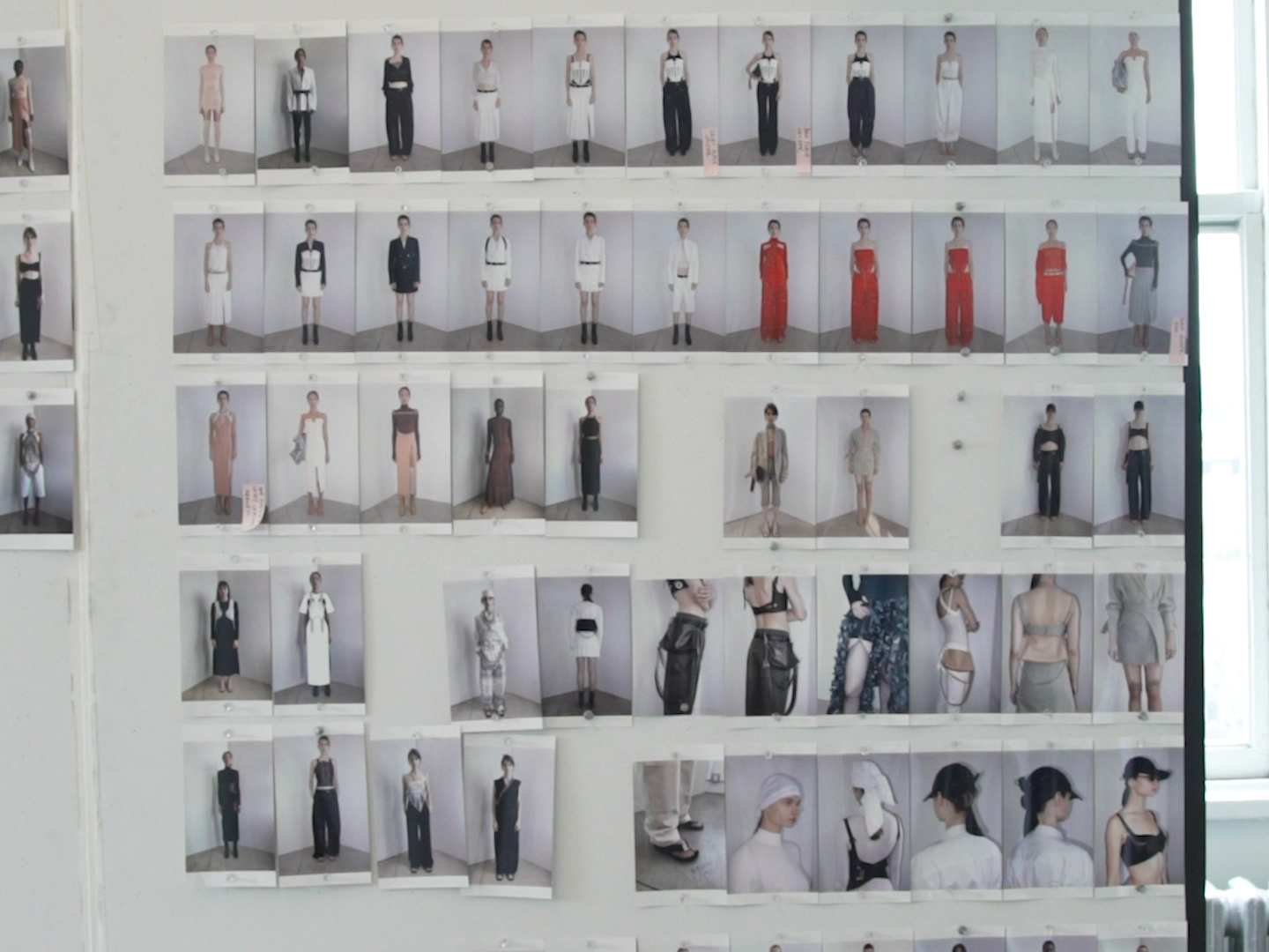 Fashion lineup photos pinned to a wall, showing multiple model looks and outfit details.