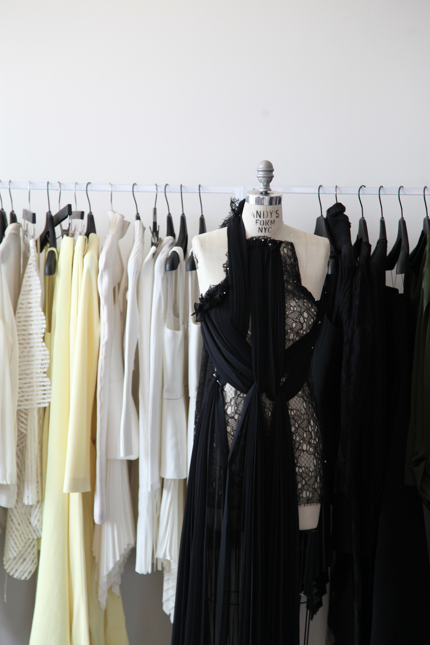  - Black dress on mannequin in front of a clothing rack with white and black garments.