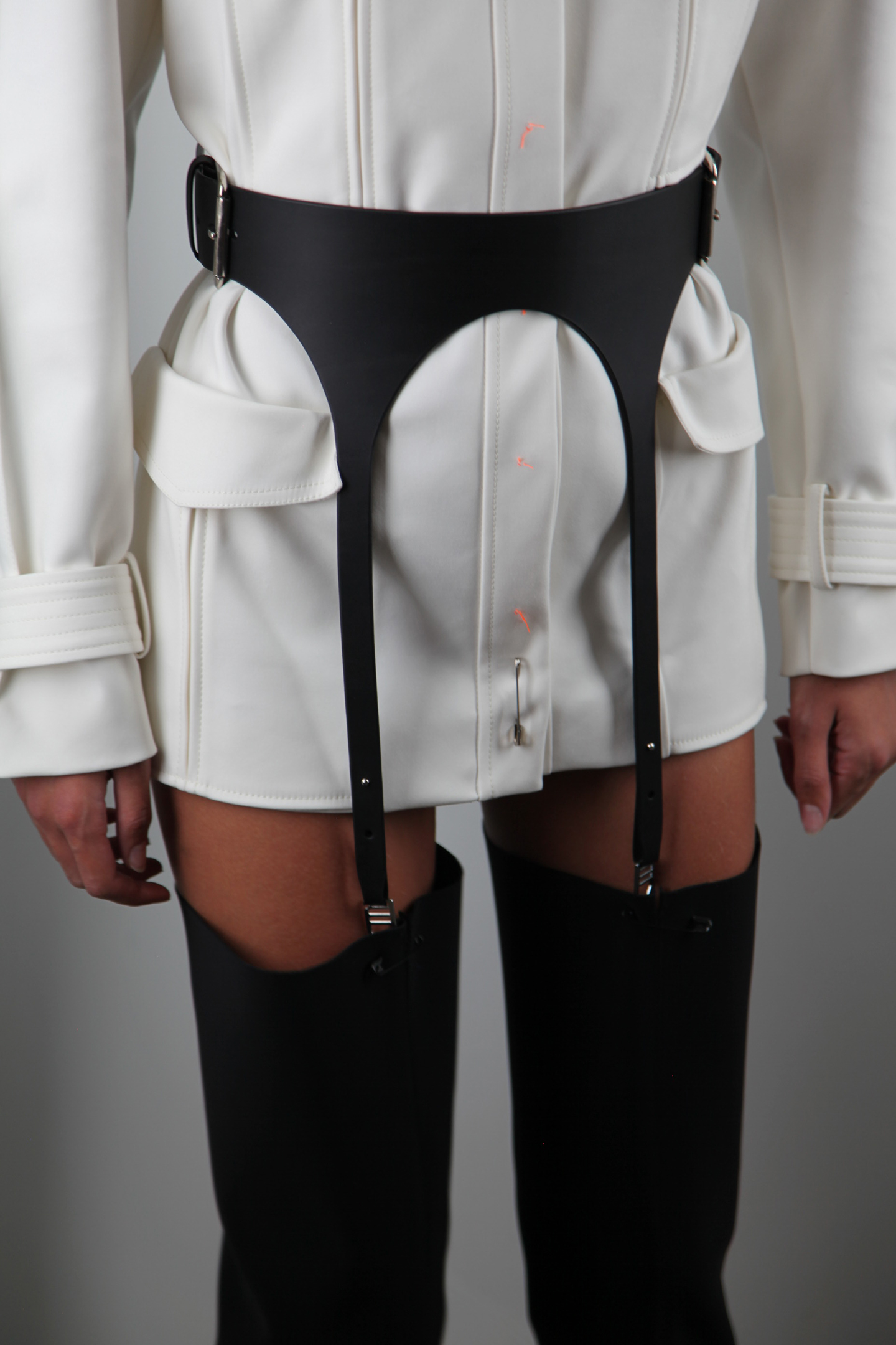 White mini dress with black harness belt and thigh-high black boots.