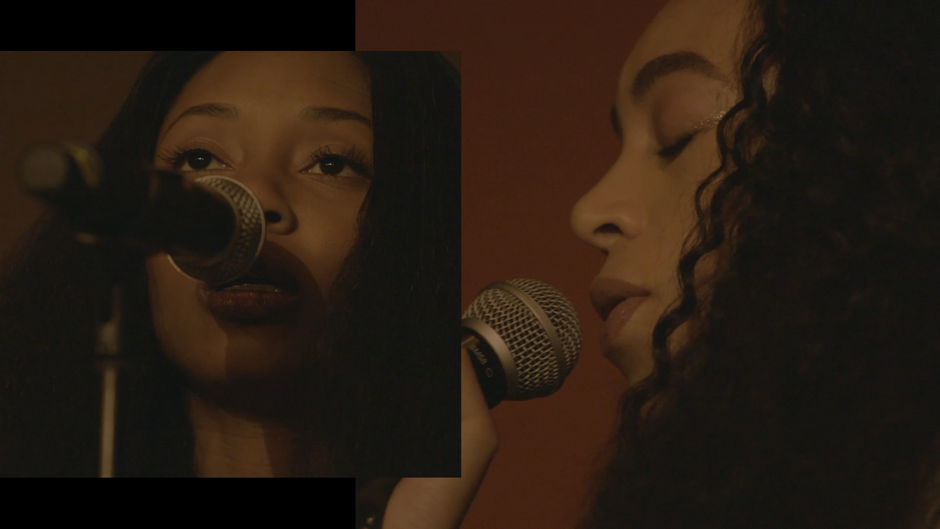 Person with long dark hair singing into a microphone in warm, dim lighting.
