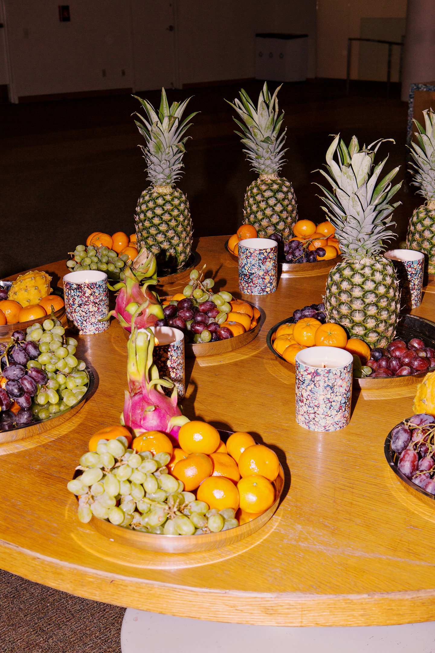  - Fruit centerpieces with pineapples, grapes, and citrus on round wooden tables.