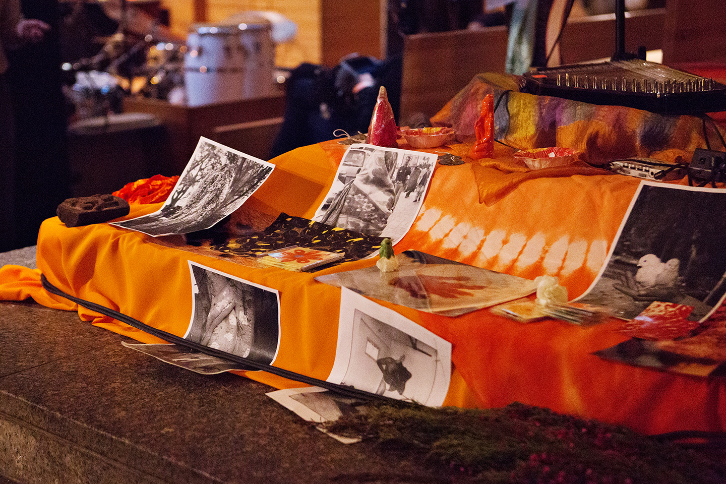  - Orange-draped display table with printed photos and small objects in a dim room.