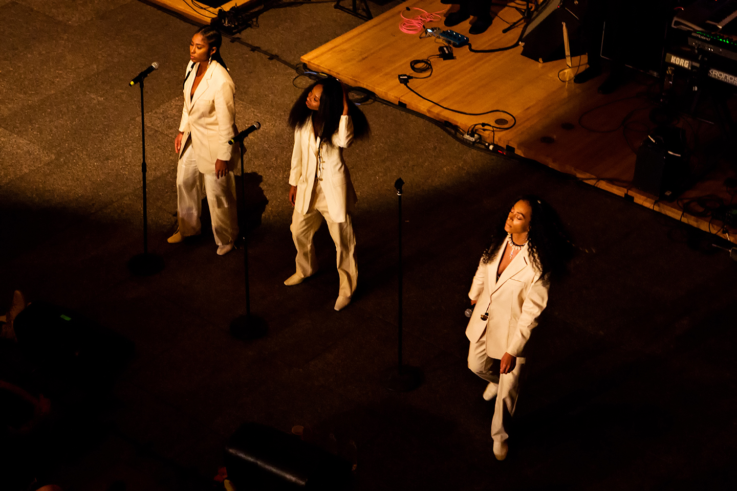 Three performers in white suits stand at microphones on a dimly lit stage.