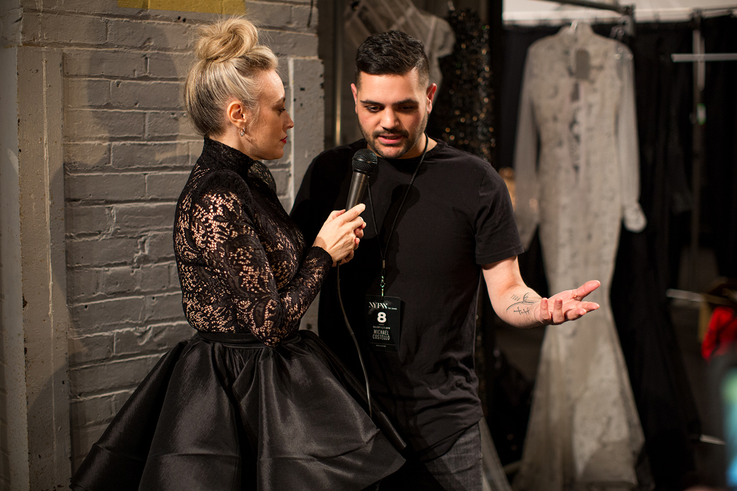 Interviewer holding a microphone to a person in black backstage.