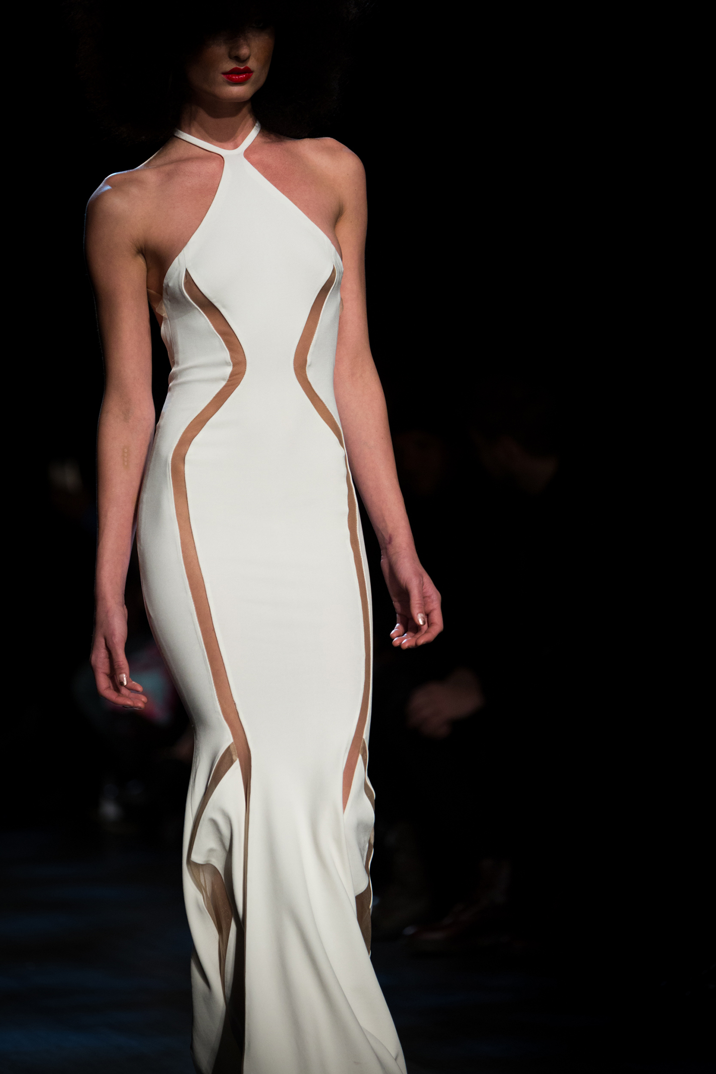Model in a white cutout halter gown on a dark runway.