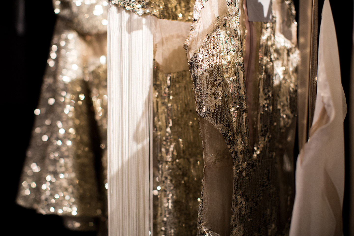Sequined dresses hanging on a rack in warm, soft lighting.
