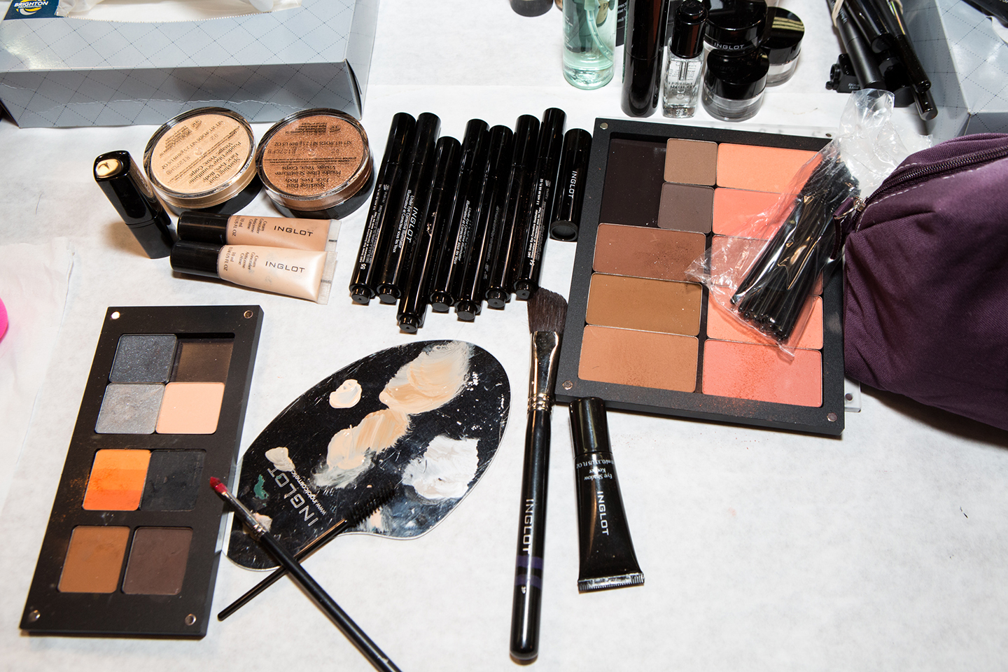 Makeup palettes, brushes, and cosmetic tubes spread across a tabletop.