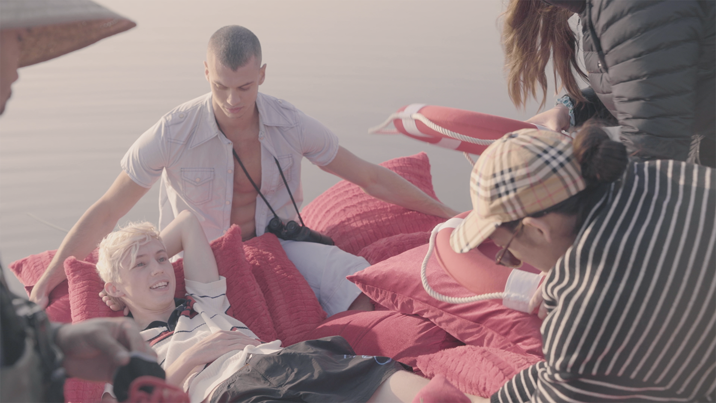 People lounging on pink cushions by wate
