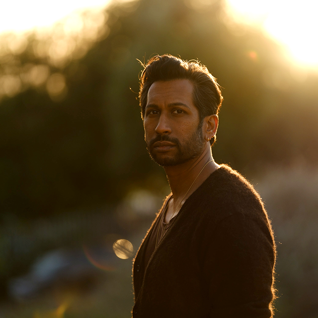 Man standing beside a stone wall outdoors in soft natural light