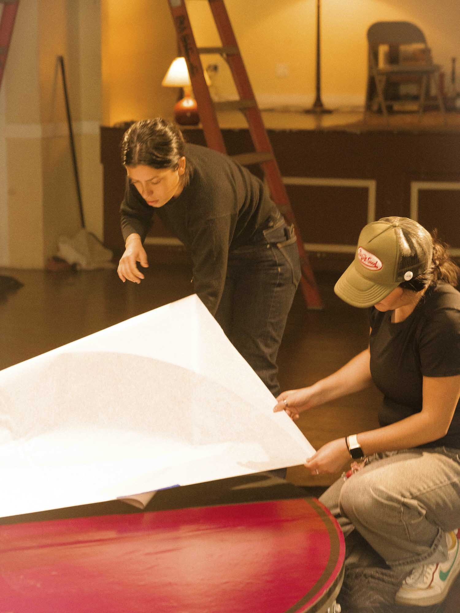  - Two crew members position large sheet of material over platform during production setup