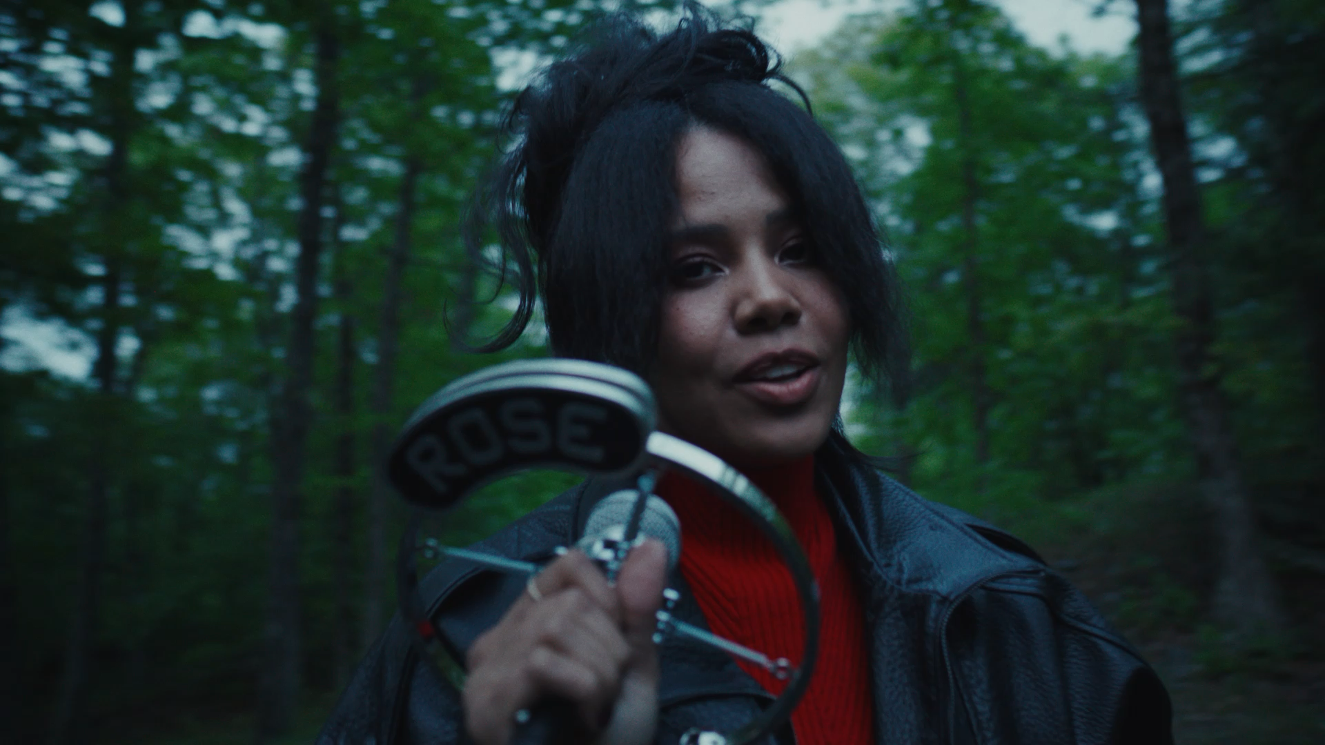  - Baby Rose holds a handheld microphone while standing in wooded setting