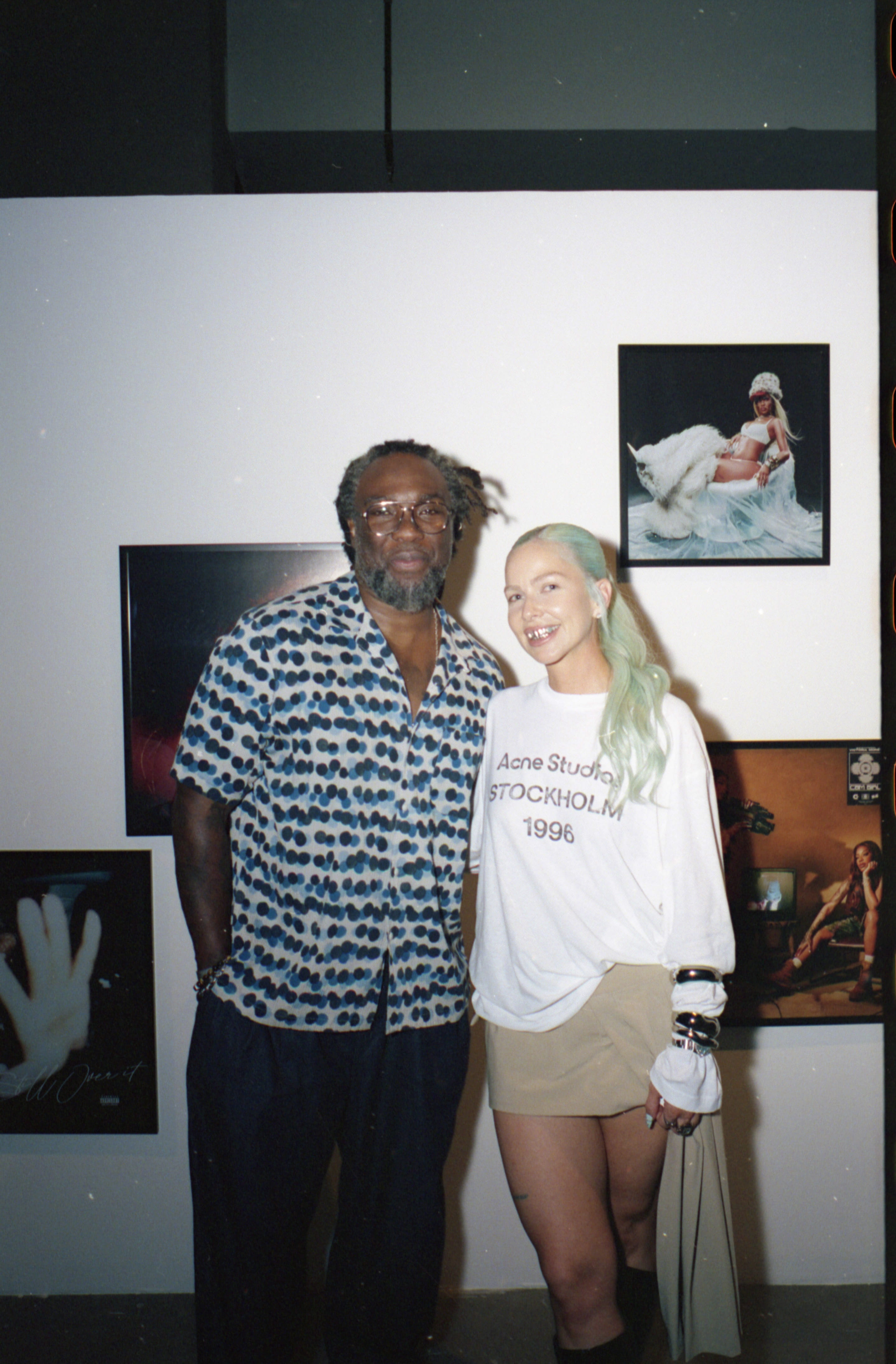 Two people pose together in front of photographs displayed on gallery wall