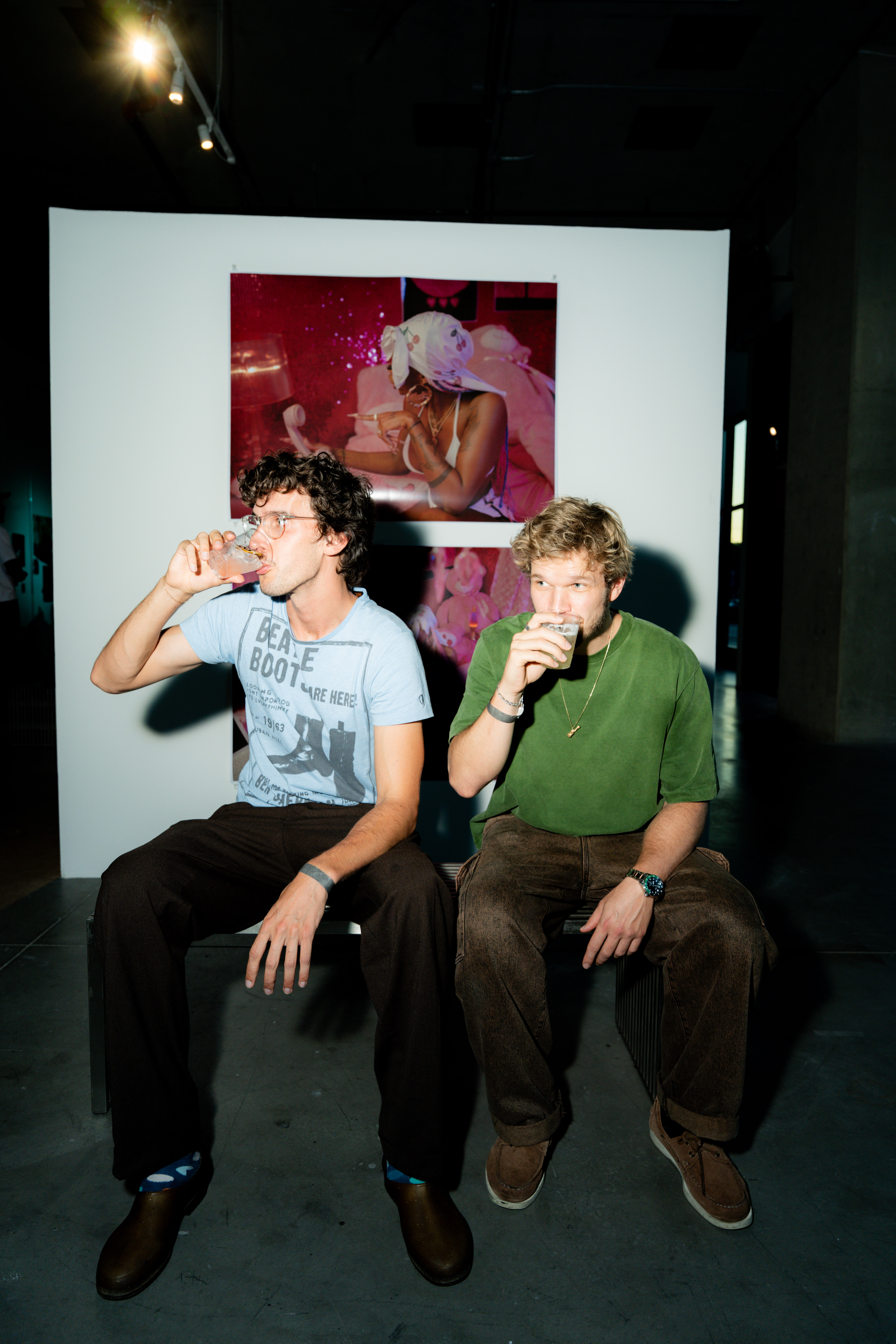 Two people sit drinking from cups in front of photographs displayed at the exhibition